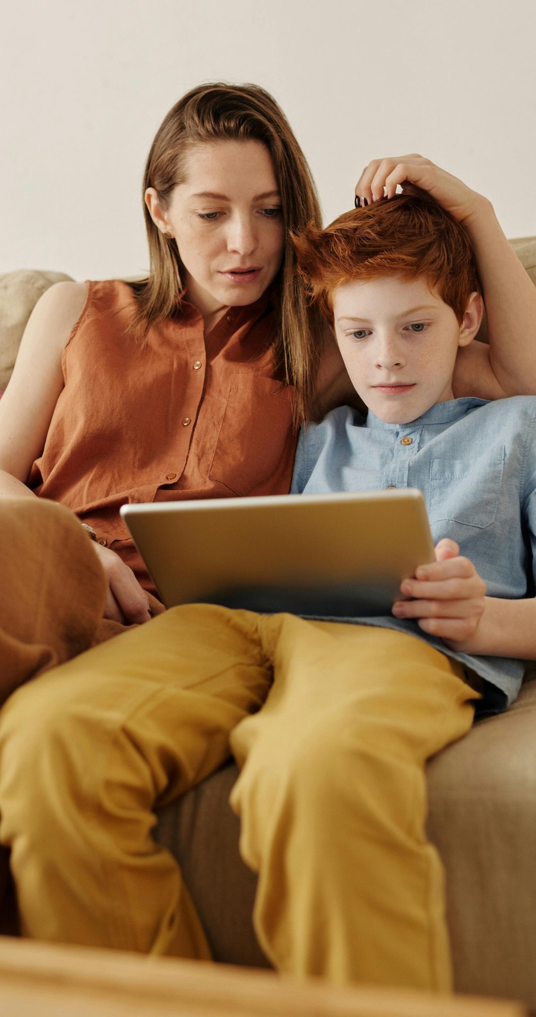 Mother and son sitting on a couch together looking at a tablet