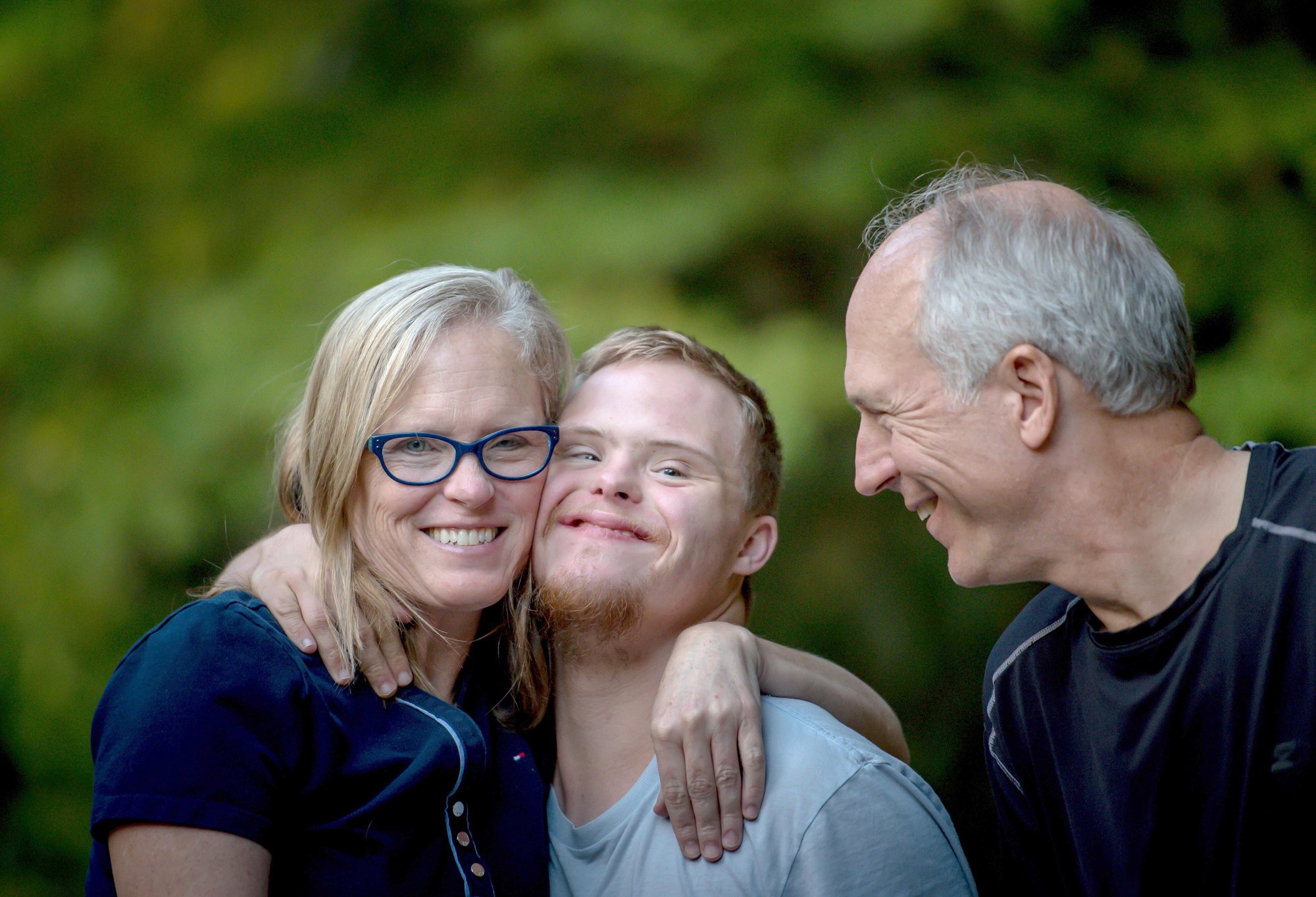 Mother hugs son while dad looks on, smiling